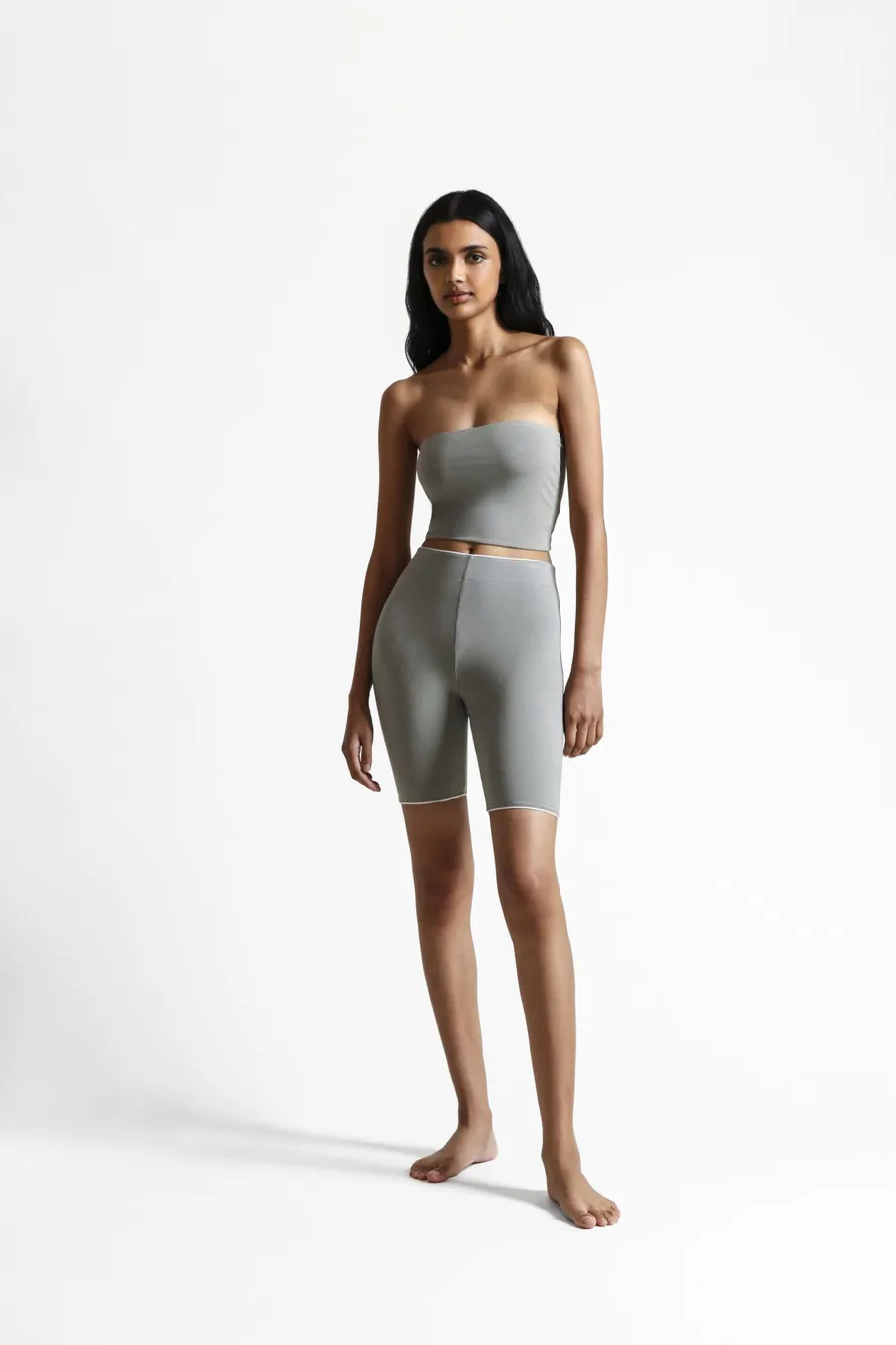 Full-length: model in a sage tube top and bike shorts standing barefoot on a white ground