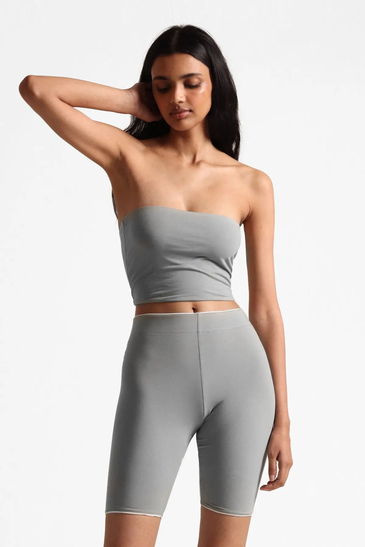 Model in a sage tube top and bike shorts, one arm raised behind her head
