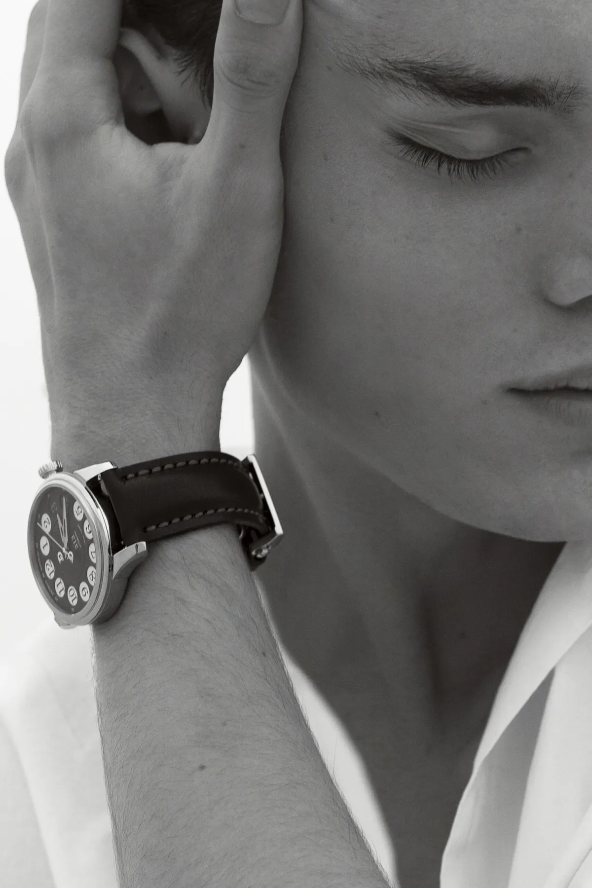 Black and white close-up: man with his hand over his eyes, a leather-strap watch on his wrist