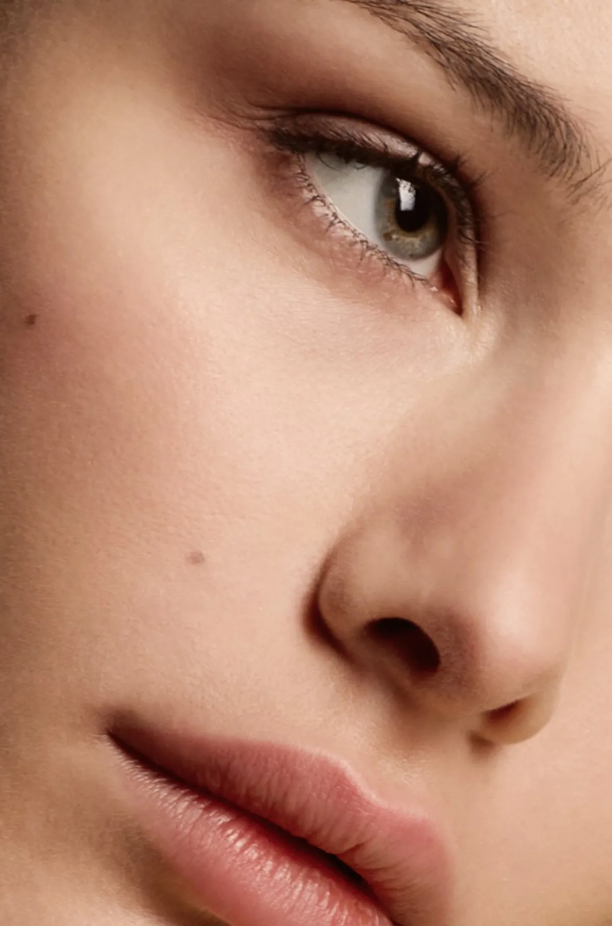 Close crop of a model’s eye and cheek, freckles and lashes in soft light