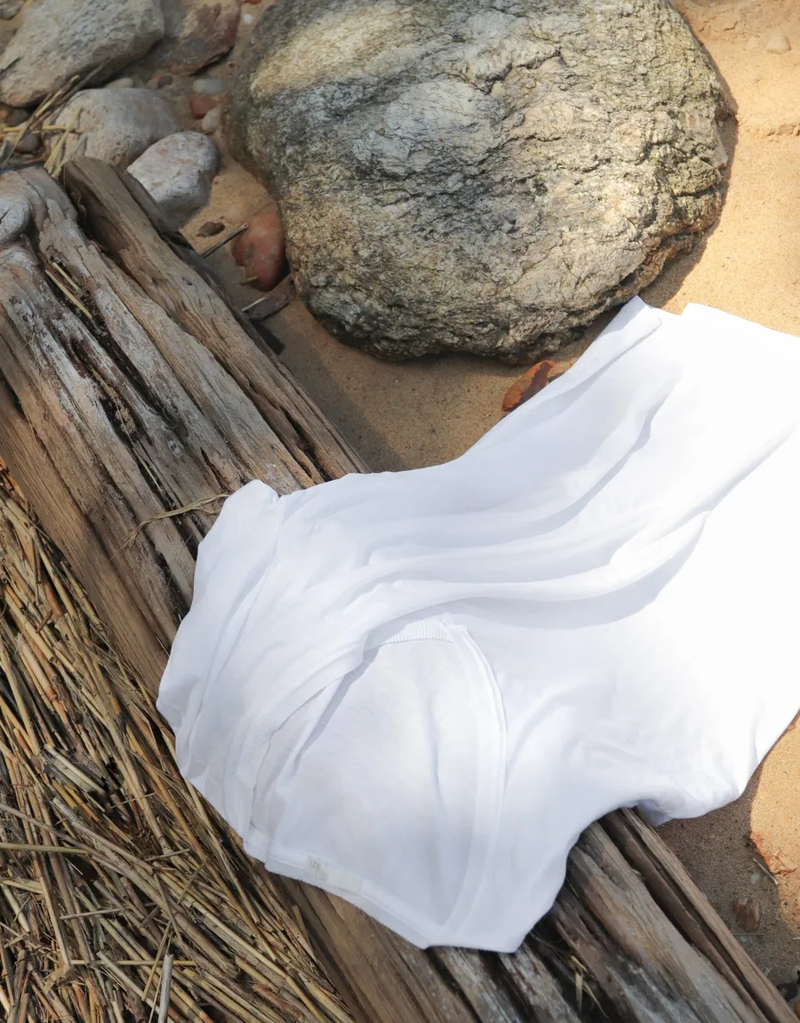 White fabric draped over driftwood with a rounded stone, on sand